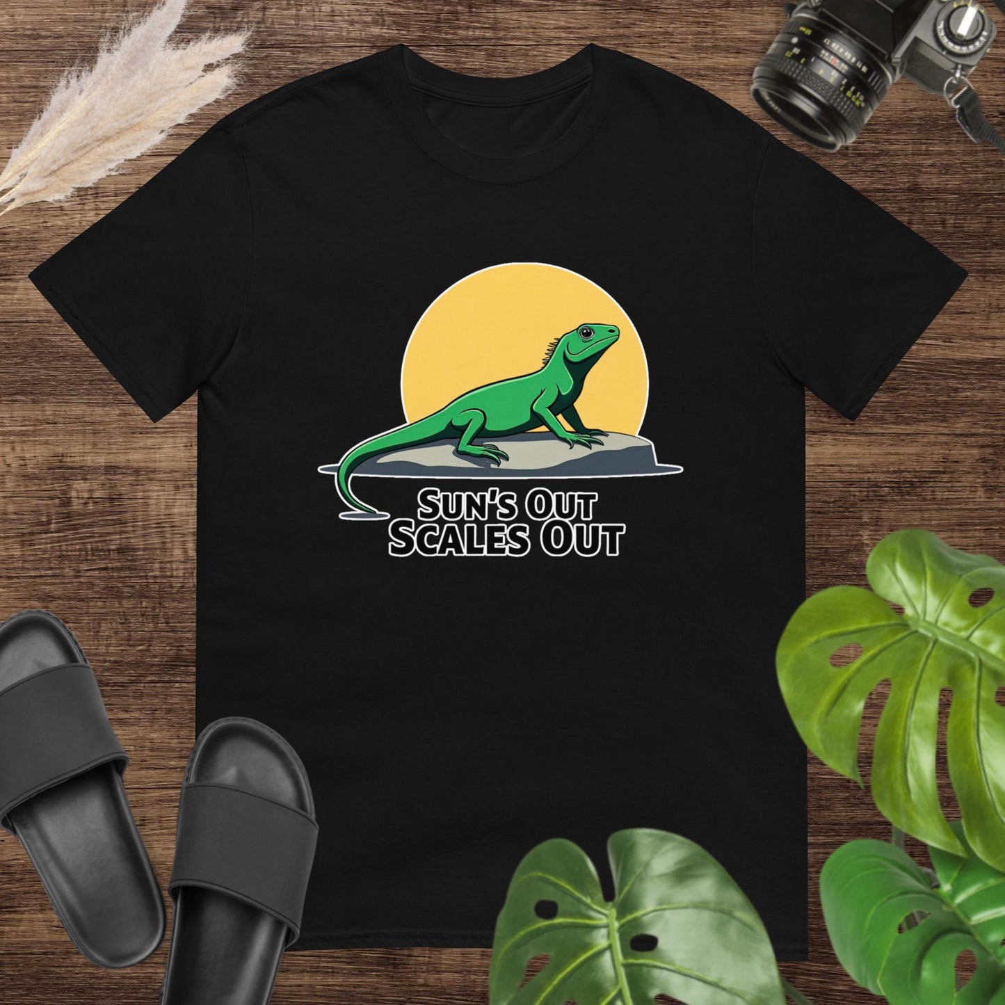 Black t-shirt featuring a green lizard on a rock with a sun and the text “Sun’s Out Scales Out.”