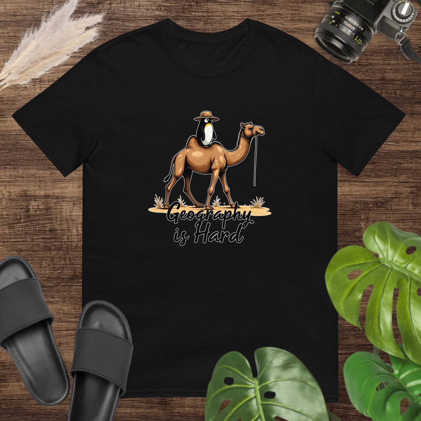 Unisex black t-shirt featuring a camel with a penguin on top and the text Geography is Hard.