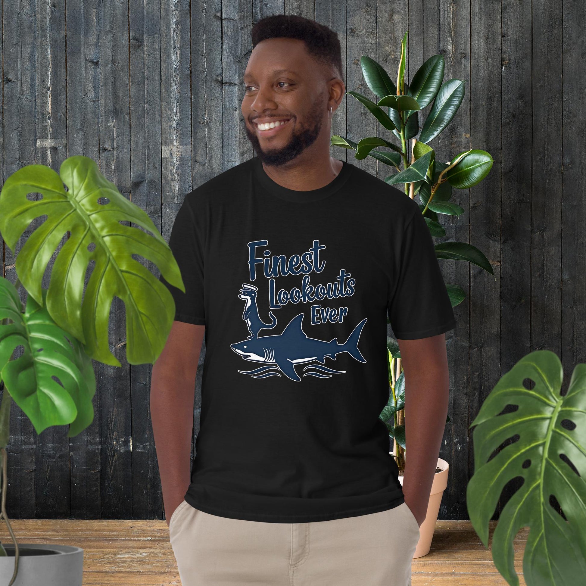 Man wearing black unisex t-shirt with 'Finest Lookouts Ever' graphic of shark and otter, 100% ring-spun cotton