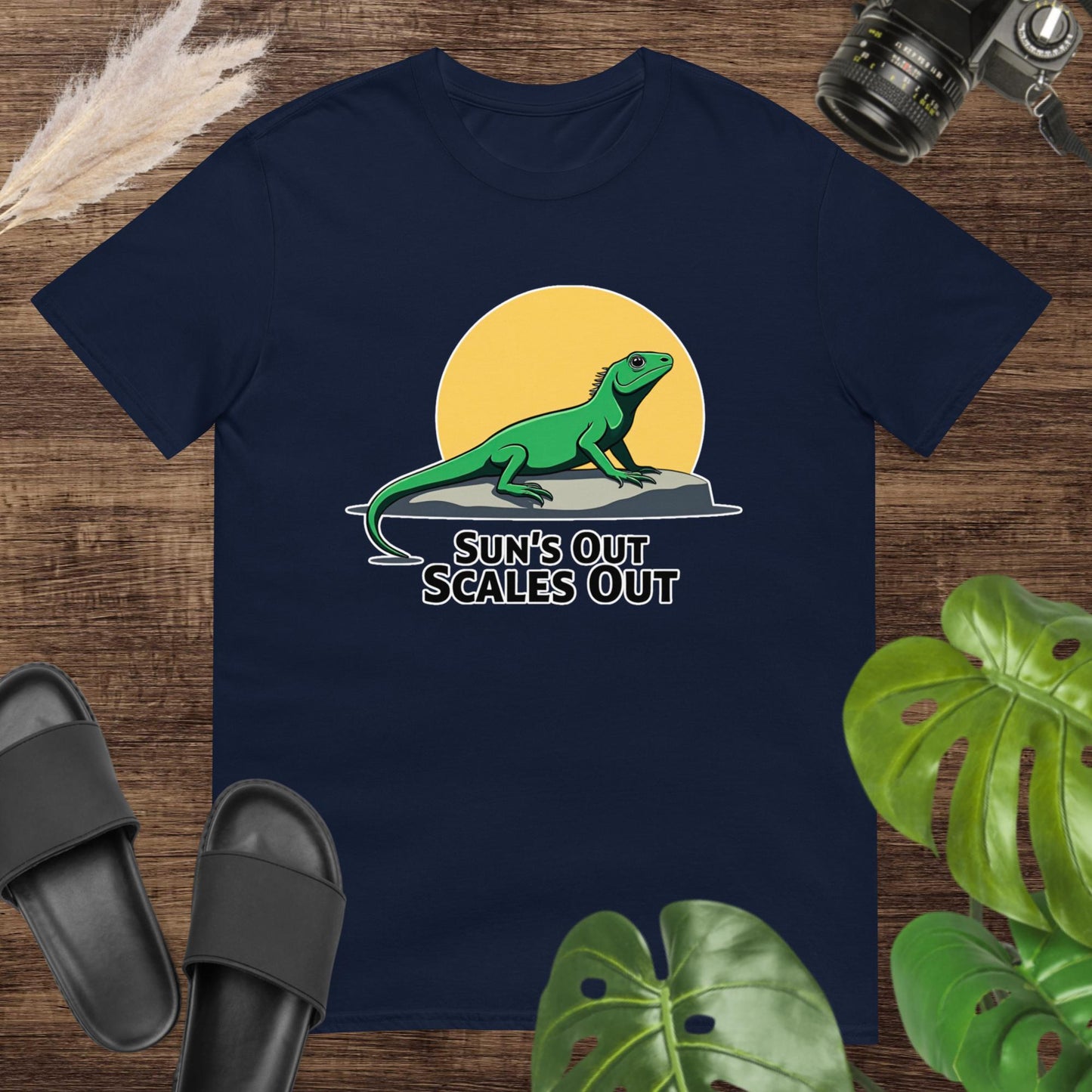 Navy  t-shirt featuring a green lizard on a rock with a sun and the text “Sun’s Out Scales Out.”