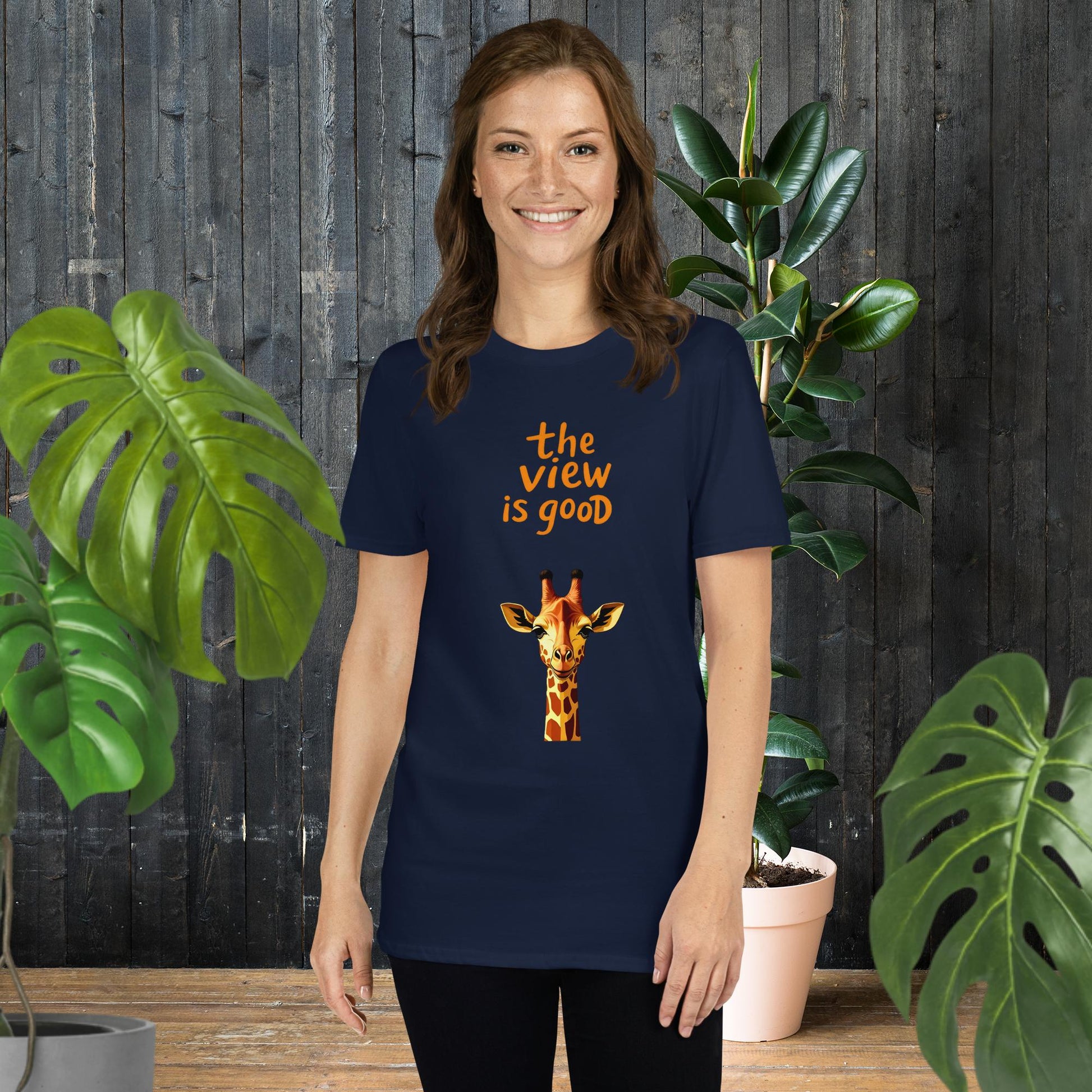 Woman wearing navy t-shirt with giraffe graphic and 'the view is good' text, surrounded by plants