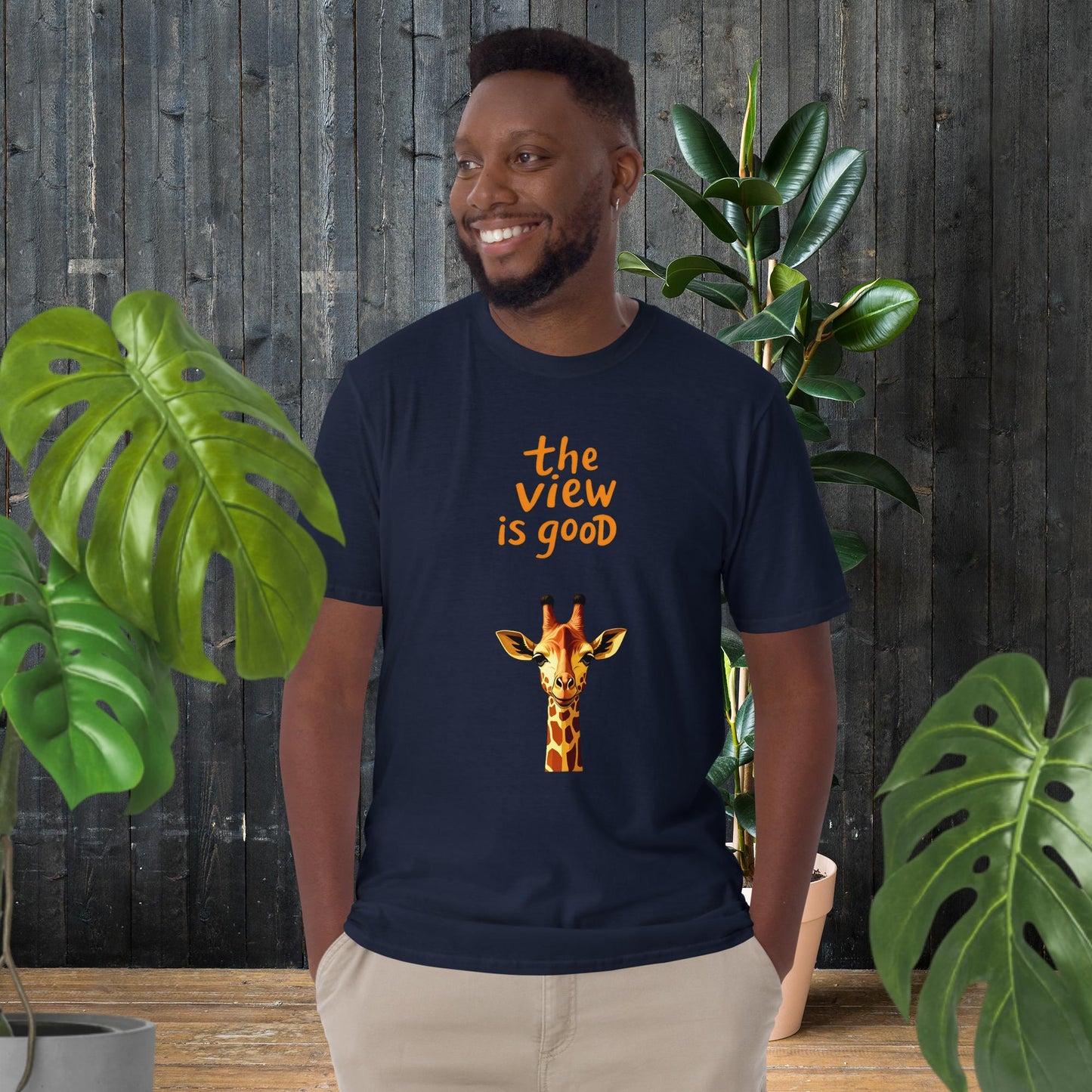 Man wearing navy t-shirt with giraffe graphic and 'the view is good' text, surrounded by plants