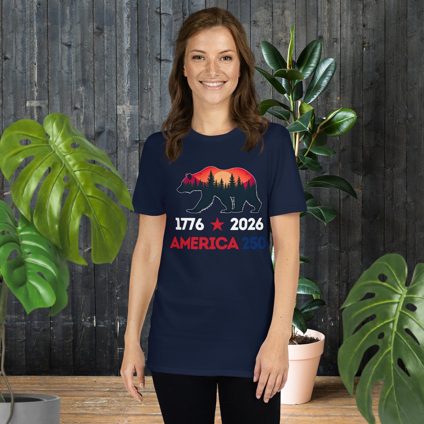 Woman wearing navy t-shirt with bear silhouette, forest sunset, and 'America 250' text for 1776-2026 celebration