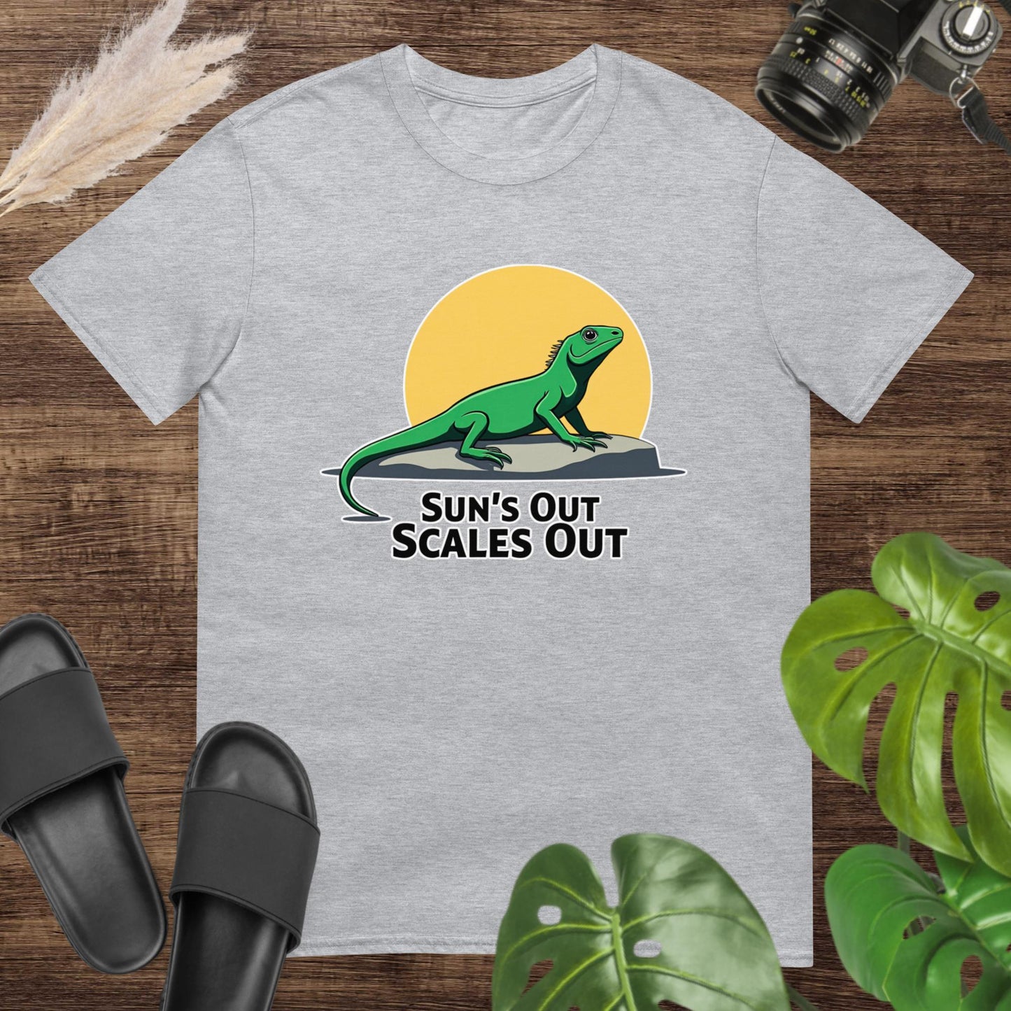 Grey t-shirt featuring a green lizard on a rock with a sun and the text “Sun’s Out Scales Out.”
