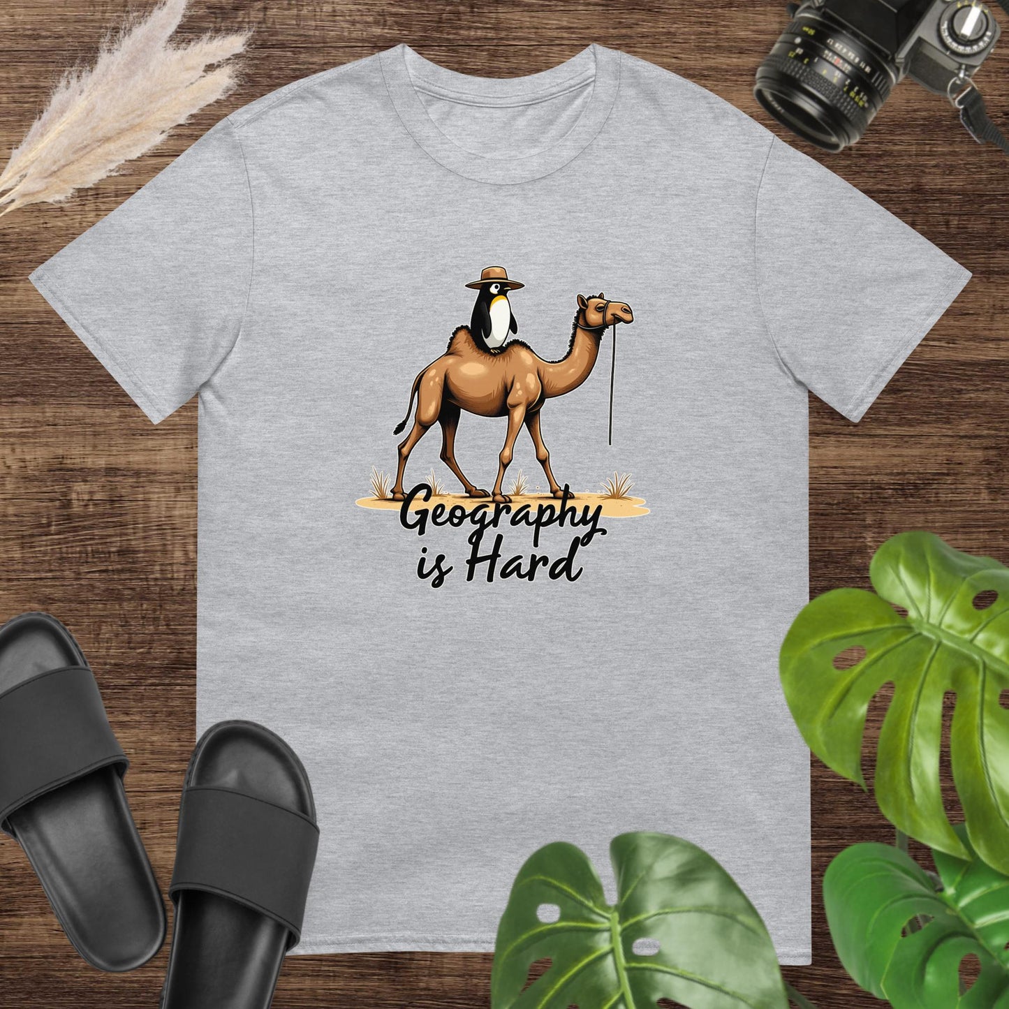 Unisex grey t-shirt featuring a camel with a penguin on top and the text Geography is Hard.