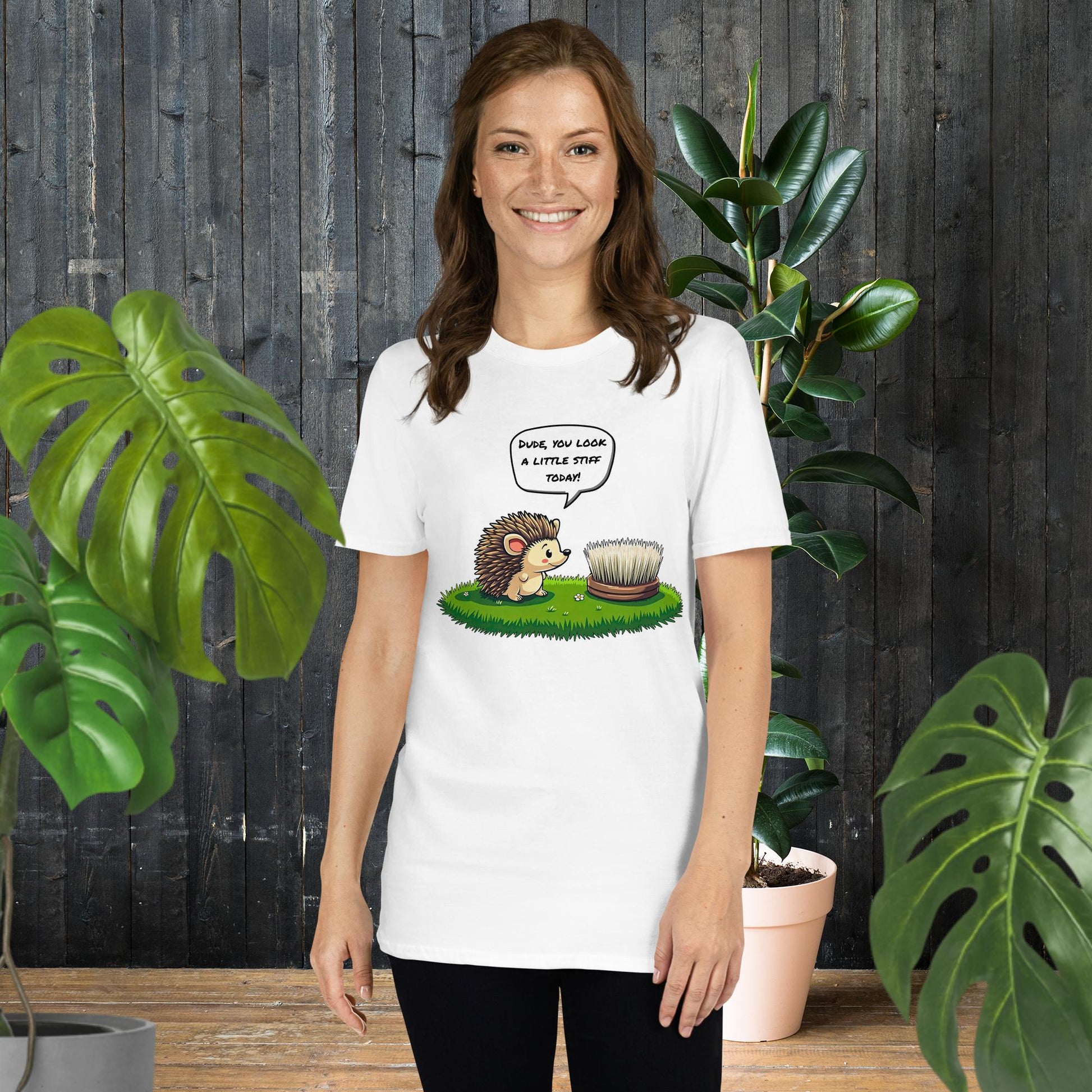 Woman wearing funny hedgehog graphic tee with 'Dude, you look a little stiff today!' caption, surrounded by plants.